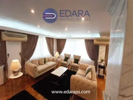Living room with beige tufted sofas, armchairs, and a coffee table, featuring soft lighting and elegant decor.