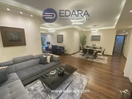 Modern living room with a gray sectional sofa, wooden flooring, and contemporary lighting fixtures.
