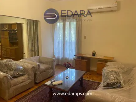 Living room with two sofas covered in plastic, a wooden table, and a window with curtains.