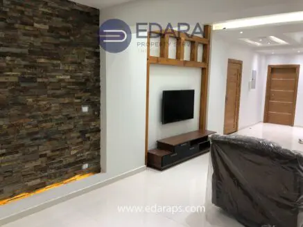 Modern living room with a stone accent wall, television unit, and minimalist furniture design.