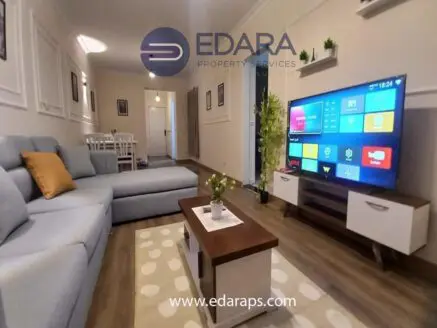 Modern living room with a gray sectional sofa, coffee table, and large TV displaying various apps.