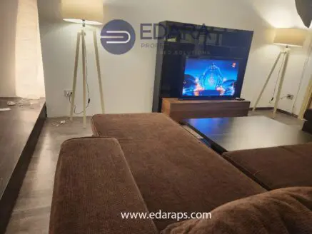 Living room interior with a brown sofa, coffee table, and a television displaying a performance.