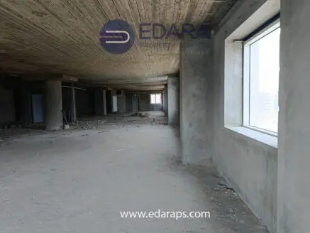 Interior view of an unfinished commercial space with concrete walls and flooring, featuring large windows.