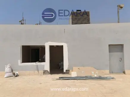 Exterior view of a building under renovation with an open window and construction materials visible.