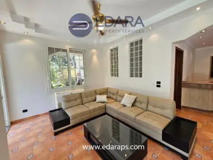 Modern living room with a beige sectional sofa and a glass coffee table in a well-lit space.