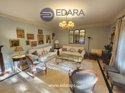 Living room with a white sofa, armchairs, and framed artwork on the walls in a well-lit space.