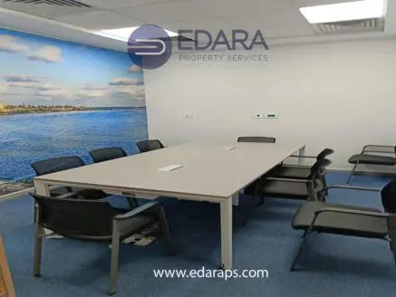 Conference room with a large table and several chairs arranged around it, featuring a coastal mural on the wall.