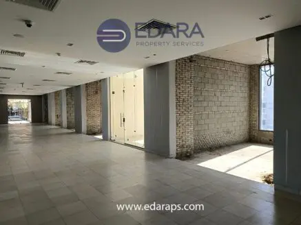 Interior view of an unfinished commercial space with large glass doors and exposed brick walls.
