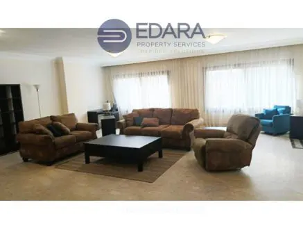 Living room with brown sofas, a coffee table, and large windows allowing natural light.