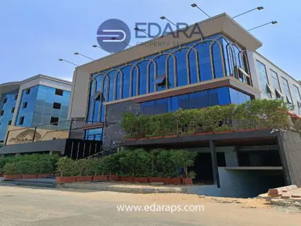 Contemporary commercial building featuring large glass windows and greenery at the entrance.