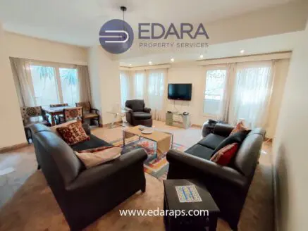 Living room with two black leather sofas, a coffee table, and a television in a well-lit space with large windows.