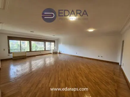 Spacious empty living room with wooden flooring and large windows allowing natural light.