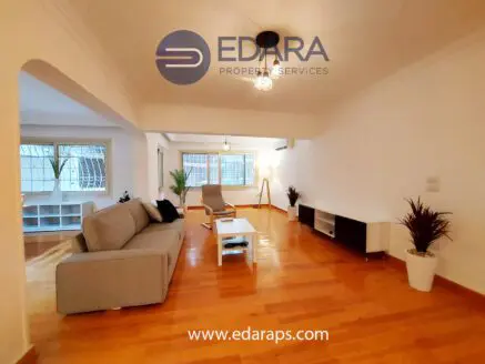 Living room with a gray sofa, wooden flooring, and modern furniture in a bright space.