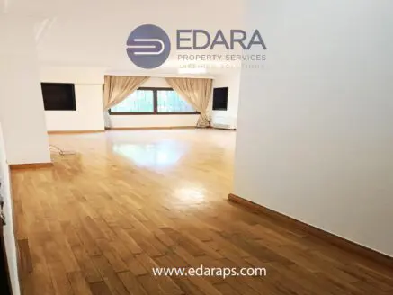 Spacious interior of a room with wooden flooring and large windows allowing natural light.