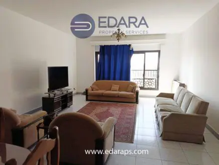 Living room with beige sofas, a television, and a blue curtain in a bright space.