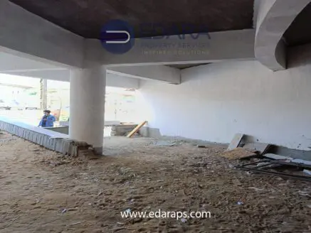 Interior view of an unfinished construction site with exposed concrete pillars and debris on the ground.