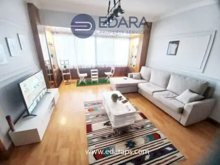 Contemporary living room featuring a light-colored sofa, a television, and a decorative rug.