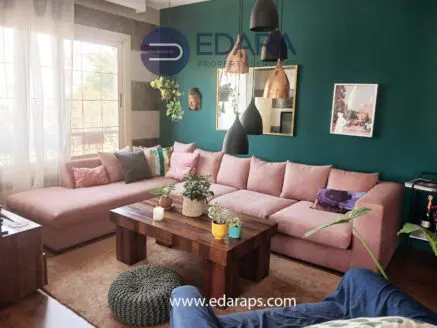 A modern living room featuring a pink sectional sofa, wooden coffee table, and decorative plants.