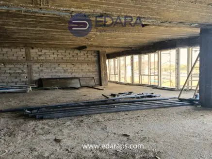 Interior view of an unfinished commercial space with exposed concrete walls and steel pipes on the floor.