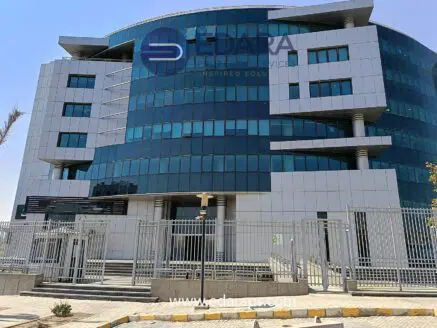 Modern office building with a glass facade and a gated entrance in a commercial area.