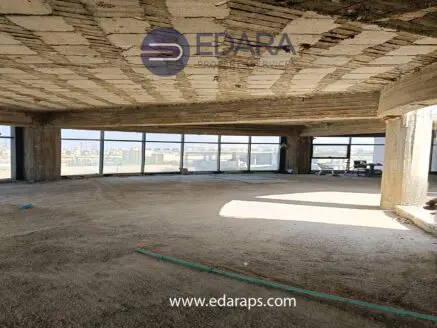 Interior view of an unfinished commercial space with large windows and exposed concrete ceiling.