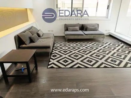Contemporary living room featuring a gray sofa, a patterned rug, and a side table in a well-lit space.