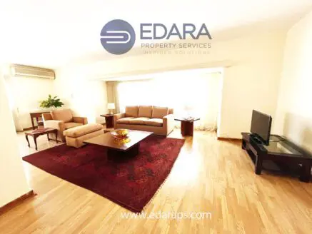 Spacious living room featuring a sofa set, coffee table, and television in a well-lit environment.