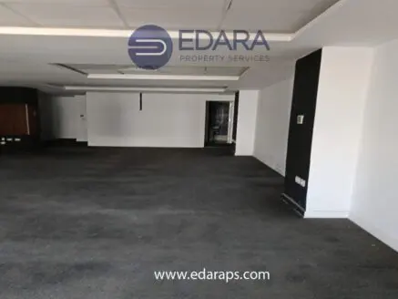 Empty commercial space with carpet flooring and white walls, featuring a ceiling with lights and a doorway.