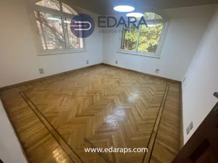 Empty room with herringbone patterned wooden flooring and large windows allowing natural light.