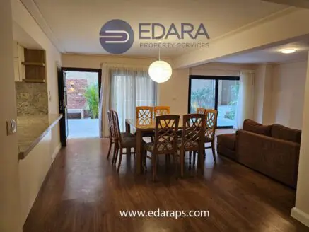 Dining area with a wooden table and chairs, featuring a sofa and large windows for natural light.