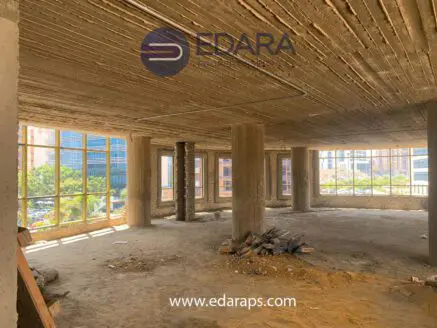 Interior view of an unfinished commercial space with exposed concrete and large windows.