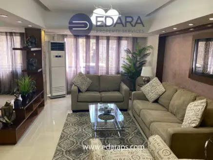 Living room featuring a beige sofa set, glass coffee table, and decorative plants in a modern interior design.