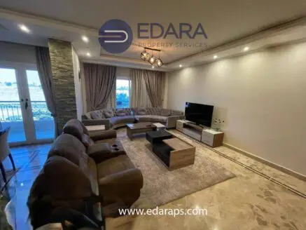 Modern living room with a large sectional sofa, coffee table, and TV, featuring neutral tones and elegant decor.