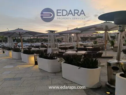 Outdoor seating area with umbrellas and planters in a commercial space during sunset.