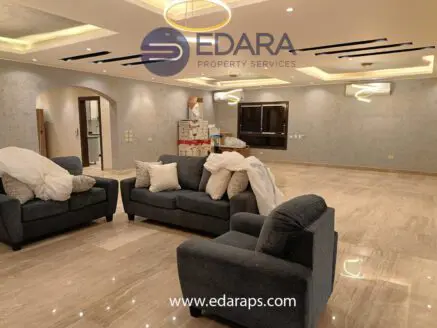 Living room with two blue sofas, white cushions, and a television mounted on the wall in a spacious interior.