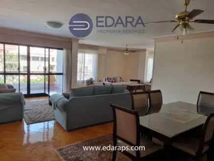Living room and dining area with light-colored furniture and large windows in a residential space.