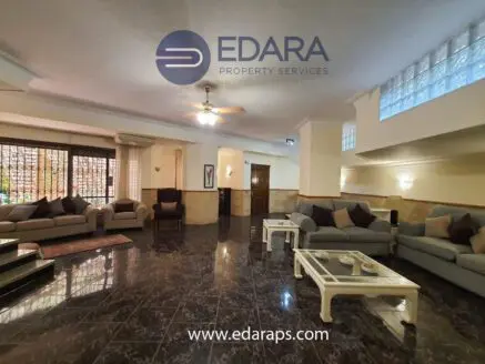 Spacious living room with multiple sofas, coffee tables, and decorative elements in a well-lit interior space.