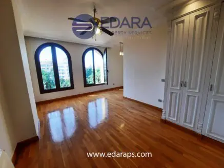 Bright interior room featuring wooden flooring and large arched windows.