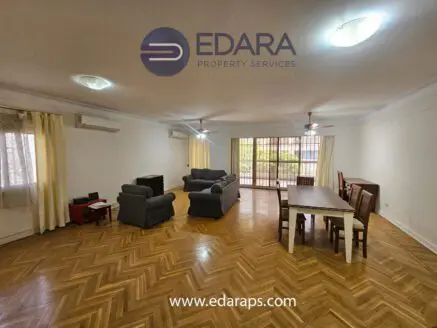 Spacious living room featuring a sofa set, dining table, and wooden flooring.