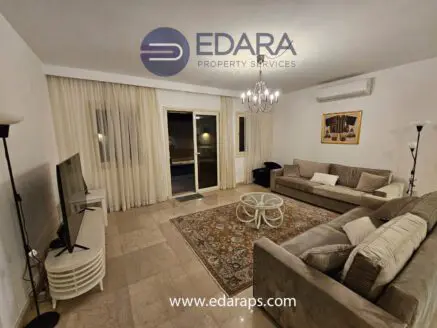 Modern living room featuring a beige sofa, television, and decorative rug in a neutral color scheme.