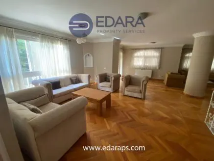 Spacious living room featuring beige sofas and a wooden coffee table on a parquet floor.
