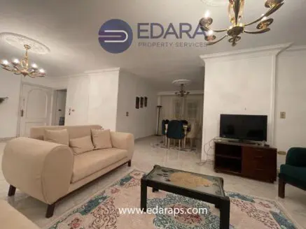 Interior view of a living room featuring a beige sofa, a television, and decorative lighting fixtures.