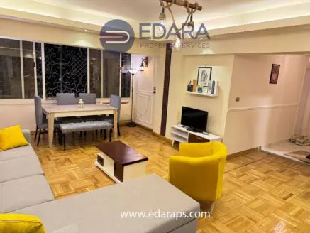 Contemporary living room featuring a gray sofa, yellow chairs, and a dining table with chairs in a well-lit space.