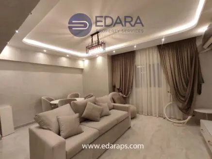 Contemporary living room with beige sofa, elegant lighting, and draped curtains in a neutral color scheme.
