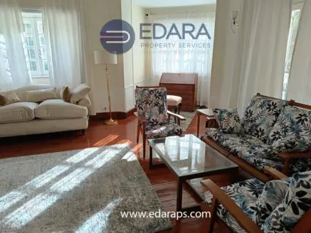 Living room featuring floral upholstered chairs, a glass coffee table, and a sofa in a well-lit space.