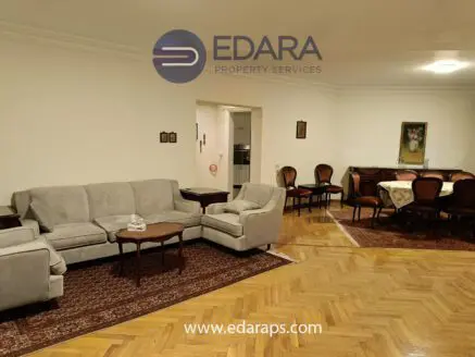 Spacious living room featuring a gray sofa, wooden coffee table, and a dining area with chairs and a table.