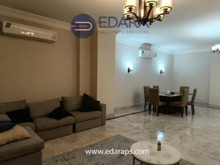 Interior view of a living room featuring a sofa and a dining table in a neutral color scheme.