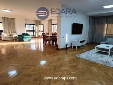 Bright living room featuring wooden flooring, a television, and various seating arrangements.