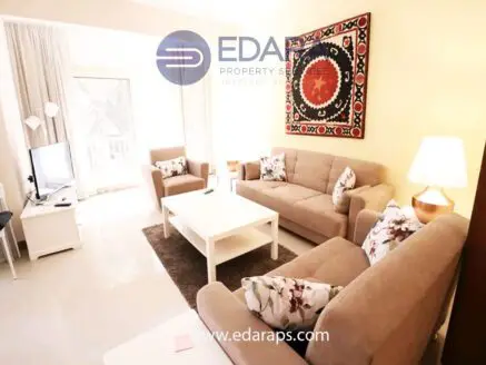 Living room featuring two beige sofas, a coffee table, and a decorative wall hanging with intricate patterns.