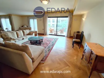 Bright living room featuring a large sofa, coffee table, and wooden furniture with a view of an outdoor balcony.